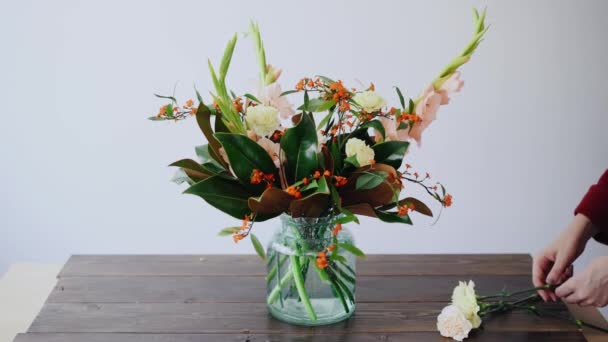 女性の花屋は、ガラスの花瓶と新しいフラワーアレンジメントを作るの花を置きます。女性ボックスから新鮮な花を摘んで花瓶に美しい花束を作成します。フラワー ショップ コンセプト — ストック動画