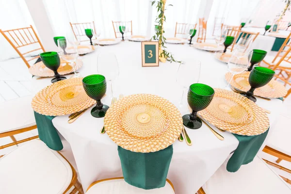 結婚式のディナー、ゲストの準備のためのテントの内部。ラウンド バンケット テーブルを提供しています。黄金料理、緑ワイン グラス、ナプキン。ケータリングのコンセプト. — ストック写真