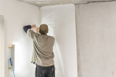 Genç adam, çalışan yapıştırma beton duvara duvar kağıtları. Daire onarın. Ev yenileme kavramı. Beyaz duvar boya için