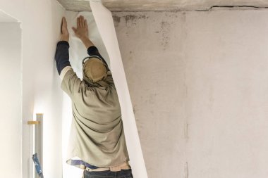 Genç adam, çalışan yapıştırma beton duvara duvar kağıtları. Daire onarın. Ev yenileme kavramı. Beyaz duvar boya için