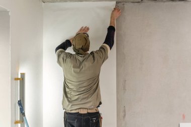 Genç adam, çalışan yapıştırma beton duvara duvar kağıtları. Daire onarın. Ev yenileme kavramı. Beyaz duvar boya için