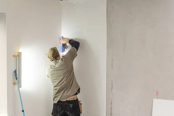Νεαρός άνδρας, εργαζόμενος συγκόλληση ταπετσαρίες τοίχου από σκυρόδεμα. Επιδιορθώσετε το διαμέρισμα. Έννοια της εγχώριας ανακαίνισης. Λευκό ταπετσαρία για το χρώμα — Φωτογραφία Αρχείου