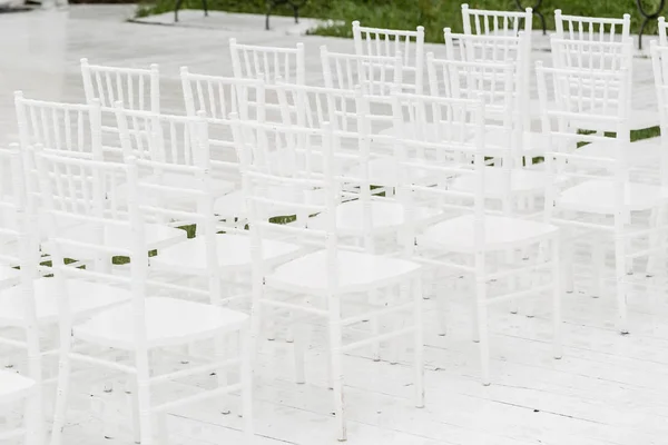 Reihen leerer weißer Stühle sitzen auf einem Holzboden. Hochzeitsstühle mit Blumen bei Zeremonie im Freien — Stockfoto