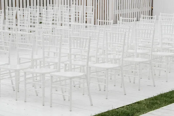 Reihen leerer weißer Stühle sitzen auf einem Holzboden. Hochzeitsstühle mit Blumen bei Zeremonie im Freien — Stockfoto