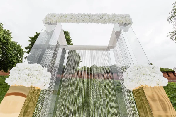 結婚式は、豪華な装飾のクリスタルの装飾です。背景の緑の芝生の上の透明なビーズの鎖で飾られた美しいアーチ — ストック写真