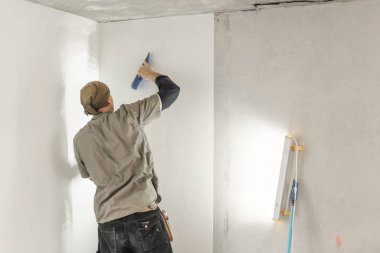 Genç adam, çalışan yapıştırma beton duvara duvar kağıtları. Daire onarın. Ev yenileme kavramı. Beyaz duvar boya için