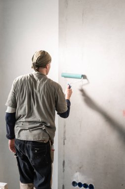 Genç adam, çalışan yapıştırma beton duvara duvar kağıtları. Daire onarın. Ev yenileme kavramı. Beyaz duvar boya için