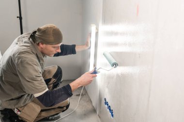 Genç adam, çalışan yapıştırma beton duvara duvar kağıtları. Daire onarın. Ev yenileme kavramı. Beyaz duvar boya için