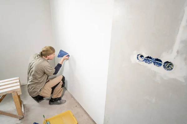 Молодий чоловік, працівник приклеює шпалери на бетонну стіну. Ремонт квартири. Концепція ремонту будинку. Білі шпалери для фарби — стокове фото