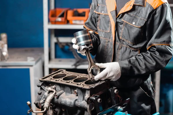 Mecánico de coche con un nuevo pistón para el motor, revisión.. Motor en un soporte de reparación con pistón y varilla de conexión de la tecnología automotriz. Interior de un taller de reparación de automóviles . — Foto de Stock