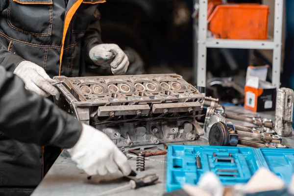 Dos mecánicos desmontando el motor, revisión.. Motor en un soporte de reparación con pistón y varilla de conexión de la tecnología automotriz. Interior de un taller de reparación de automóviles . — Foto de Stock