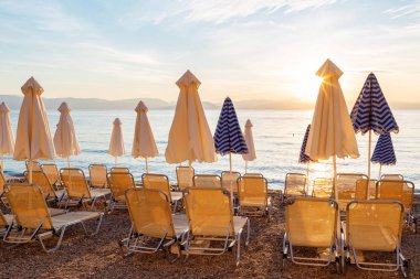 Sahilde yaz gündoğumu, Korfu Adası, Yunanistan. Anakara Yunanistan Dağları 'nın mükemmel manzarasına sahip şezlong ve şemsiyeler ile plaj.
