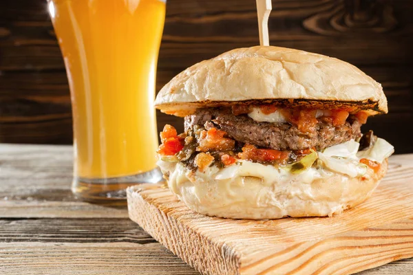 Una gran hamburguesa con carne de res cocinada sobre carbón. Almuerzo con vaso de cerveza sobre fondo de madera. El concepto de comida rápida y comida poco saludable — Foto de Stock