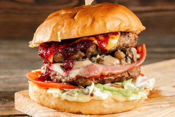 Una hamburguesa grande con dos chuletas de ternera, cocinadas a carbón. Almuerzo sobre fondo de madera. El concepto de comida rápida y no saludable — Foto de Stock