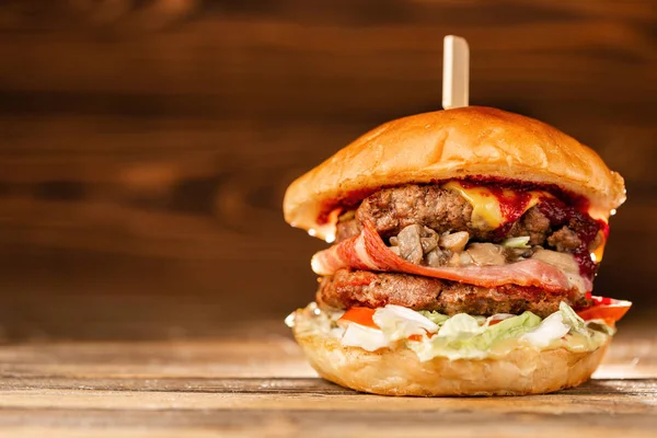 Una hamburguesa grande con dos chuletas de ternera, cocinadas a carbón. Almuerzo sobre fondo de madera. El concepto de comida rápida y no saludable — Foto de Stock