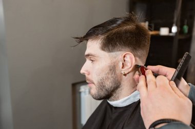 Berber makinesi ile berber işi. Profesyonel düzeltici aracı berber salonunda genç adam sakal ve saç keser.