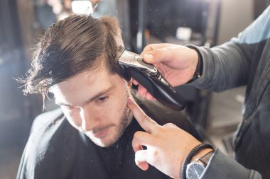 Usta berber dükkanında erkeklerin saç ve sakal keser, kuaför genç bir adam için saç modeli yapar. Berber dükkanında makas makinesi ile berber çalışması.