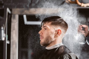 Berber, berber dükkanında kafasına temiz su püskürtüyor. Profesyonel düzeltici aracı berber dükkanı salonda genç adam üzerinde sakal ve saç keser.