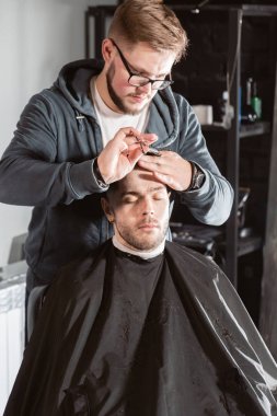 Metal makas ile saç kesimi. Usta saç ve berber erkek sakal keser, Kuaför genç bir adam için saç modeli yapar