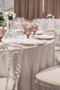 Yuvarlak ziyafet masasında şarap kadehi servis edilir. Düğün yemeği için restoranın içinde, misafirler için hazır. Çiçek aranjmanıyla süslenmiş. Tabaklar, şarap bardakları ve peçeteler. Yemek konsepti.