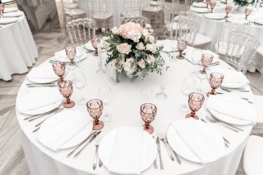 Yuvarlak ziyafet masası servis edildi. Düğün yemeği için restoranın içinde, misafirler için hazır. Çiçek aranjmanıyla süslenmiş. Tabaklar, şarap bardakları ve peçeteler. Yemek konsepti.