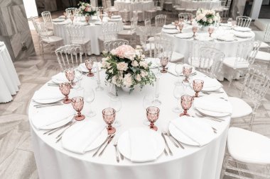 Yuvarlak ziyafet masası servis edildi. Düğün yemeği için restoranın içinde, misafirler için hazır. Çiçek aranjmanıyla süslenmiş. Tabaklar, şarap bardakları ve peçeteler. Yemek konsepti.