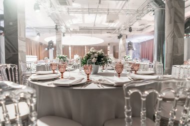 Yuvarlak ziyafet masası servis edildi. Düğün yemeği için restoranın içinde, misafirler için hazır. Çiçek aranjmanıyla süslenmiş. Tabaklar, şarap bardakları ve peçeteler. Yemek konsepti.
