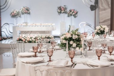 Yuvarlak ziyafet masası servis edildi. Düğün yemeği için restoranın içinde, misafirler için hazır. Çiçek aranjmanıyla süslenmiş. Tabaklar, şarap bardakları ve peçeteler. Yemek konsepti.