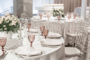 Yuvarlak ziyafet masası servis edildi. Düğün yemeği için restoranın içinde, misafirler için hazır. Çiçek aranjmanıyla süslenmiş. Tabaklar, şarap bardakları ve peçeteler. Yemek konsepti.
