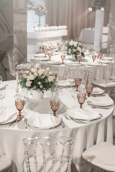 ラウンドバンケットテーブルのワイングラスが提供されます。結婚式のディナーのためのレストランのインテリア、ゲストのための準備。フラワーアレンジメントで飾られています。料理、ワイングラス、ナプキン。ケータリングのコンセプト. — ストック写真