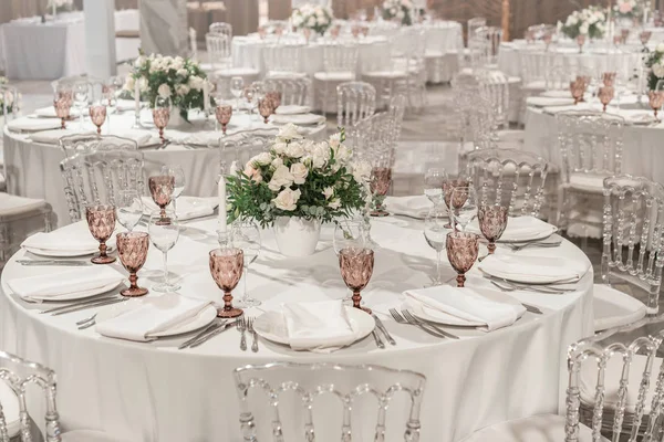 Yuvarlak ziyafet masası servis edildi. Düğün yemeği için restoranın içinde, misafirler için hazır. Çiçek aranjmanıyla süslenmiş. Tabaklar, şarap bardakları ve peçeteler. Yemek konsepti.