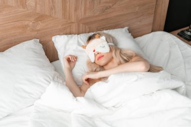 Genç bir kadın uyumak için rahat bir yatakta maske takar. Gözlerim bağlıydı. Otel odasında sabah oldu. Beyaz yastık ve battaniye
