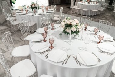 Yuvarlak ziyafet masası servis edildi. Düğün yemeği için restoranın içinde, misafirler için hazır. Çiçek aranjmanıyla süslenmiş. Tabaklar, şarap bardakları ve peçeteler. Yemek konsepti.
