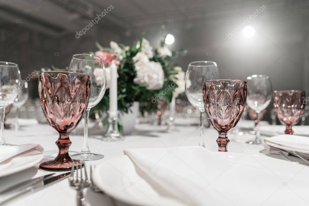 Wine glasses on round Banquet table served. Interior of restaurant for wedding dinner, ready for guests. Decorated with floral arrangement. Dishes, wine glasses and napkins. Catering concept.