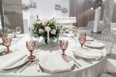 Yuvarlak ziyafet masasında şarap kadehi servis edilir. Düğün yemeği için restoranın içinde, misafirler için hazır. Çiçek aranjmanıyla süslenmiş. Tabaklar, şarap bardakları ve peçeteler. Yemek konsepti.