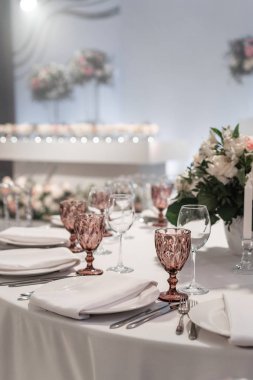 Yuvarlak ziyafet masasında şarap kadehi servis edilir. Düğün yemeği için restoranın içinde, misafirler için hazır. Çiçek aranjmanıyla süslenmiş. Tabaklar, şarap bardakları ve peçeteler. Yemek konsepti.