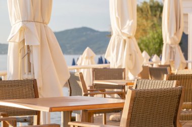 Kafede masalar. Sahilde yaz gündoğumu, Korfu Adası, Yunanistan. Anakara Yunanistan Dağları 'nın mükemmel manzarasına sahip şezlong ve şemsiyeler ile plaj.