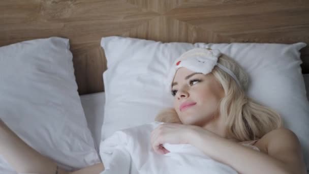 Утро в номере отеля. Молодая женщина спит на удобной кровати в маске для сна. Повязка на глаза. Белая подушка и одеяло — стоковое видео