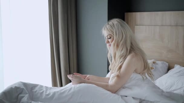 Verwenden Sie das Telefon. überprüft E-Mails und Social-Media-Nachrichten. junge Frau wacht auf, sitzt auf bequemen Bett. Morgen im Hotelzimmer. — Stockvideo