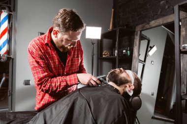 Berber dükkanında makas makinesi ile berber çalışır. Profesyonel düzeltici aracı berber dükkanı salonda genç adamın sakal ve saç keser.