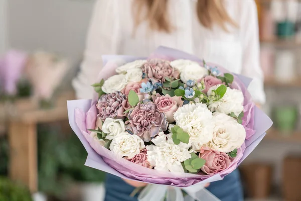 Hermoso ramo de flores mixtas en mano de mujer. el trabajo de la floristería en una florería. Delicado color pastel. Flor recién cortada. Color blanco y lila — Foto de Stock