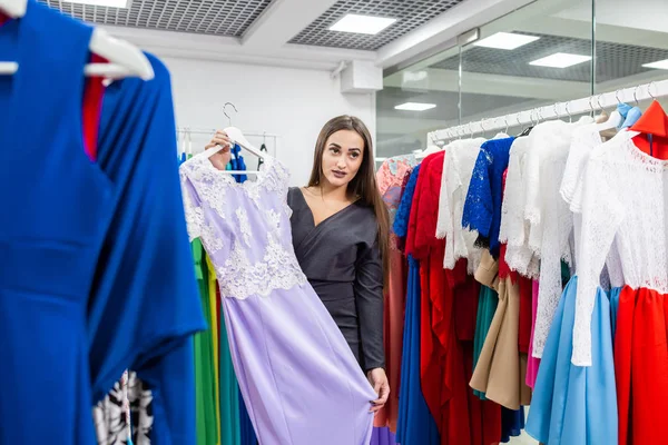 Oda arka planda ayna yakınında leylak elbise ile güzel kız. Mutlu genç kadın alışveriş merkezi veya giyim mağazasında giysi seçimi. Satış, moda, tüketicilik kavramı — Stok fotoğraf