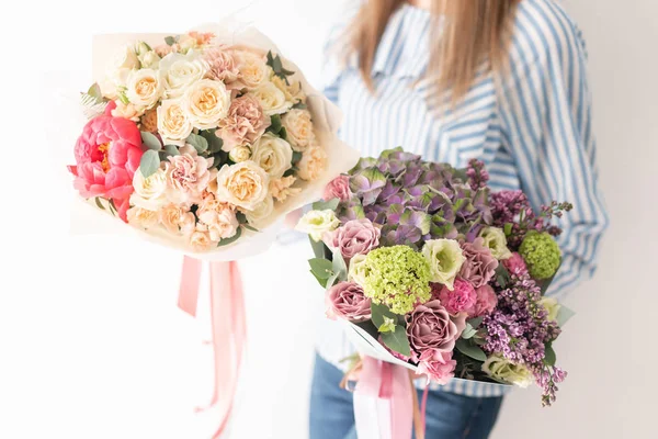 Dos hermosos ramos de flores mixtas en manos de mujeres. el trabajo de la floristería en una florería. Delicado color pastel. Flor fresca cortada . — Foto de Stock