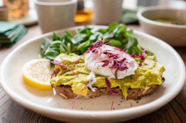 Kafede sabah, meşe masada. Avokado ile kepekli ekmek tost ile sağlıklı kahvaltı, yeşil salata ile haşlanmış yumurta. Arka Planda Yeşil çay.