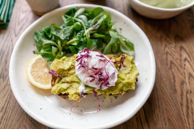 Kafede sabah, meşe masada. Avokado ile kepekli ekmek tost ile sağlıklı kahvaltı, yeşil salata ile haşlanmış yumurta. Arka Planda Yeşil çay.