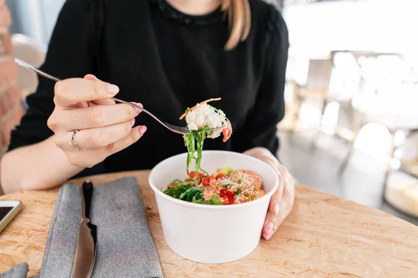 Woman eating traditional Hawaiian dish poke bowl with fork. Shrimps with rice, radish,cucumber, tomato, sesame seeds and seaweeds. Diet and Useful fast food — Stock Photo, Image