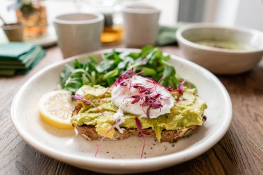 Kafede sabah, meşe masada. Avokado ile kepekli ekmek tost ile sağlıklı kahvaltı, yeşil salata ile haşlanmış yumurta. Arka Planda Yeşil çay.