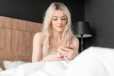 Telefonu kullan. E-posta ve sosyal medya mesajlarını denetler. Genç kadın uyanır, rahat bir yatakta oturur. Otel odasında sabah.