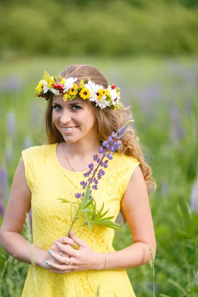 薄紫色のラインで牧草地を歩く黄色のドレスの若い女の子。暖かい夏の日。頭のための花冠 — ストック写真