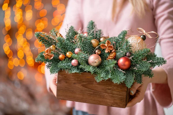Prachtige feestelijke arrangement van verse sparren met balspeelgoed in een rustieke houten doos. Kerststemming. Bokeh van Garland lichten op de achtergrond. — Stockfoto